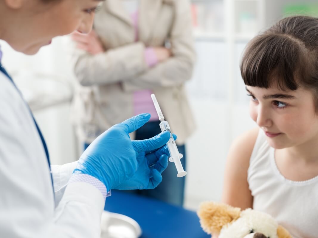 Pielęgniarka przygotowuje igłę do zabiegu biopsja dla dzieci, podczas gdy dziewczynka trzyma misia.