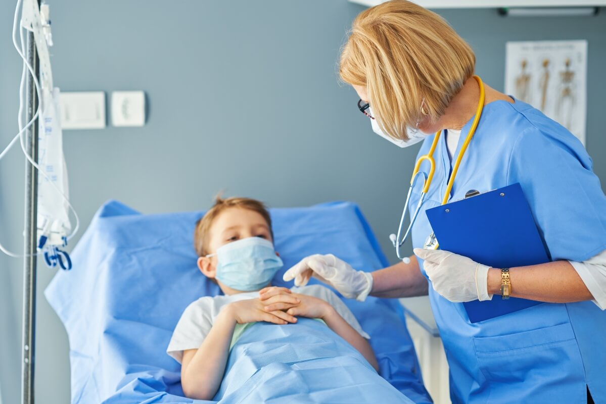 Chirurg dziecięcy rozmawia z pacjentem leżącym na łóżku szpitalnym.
