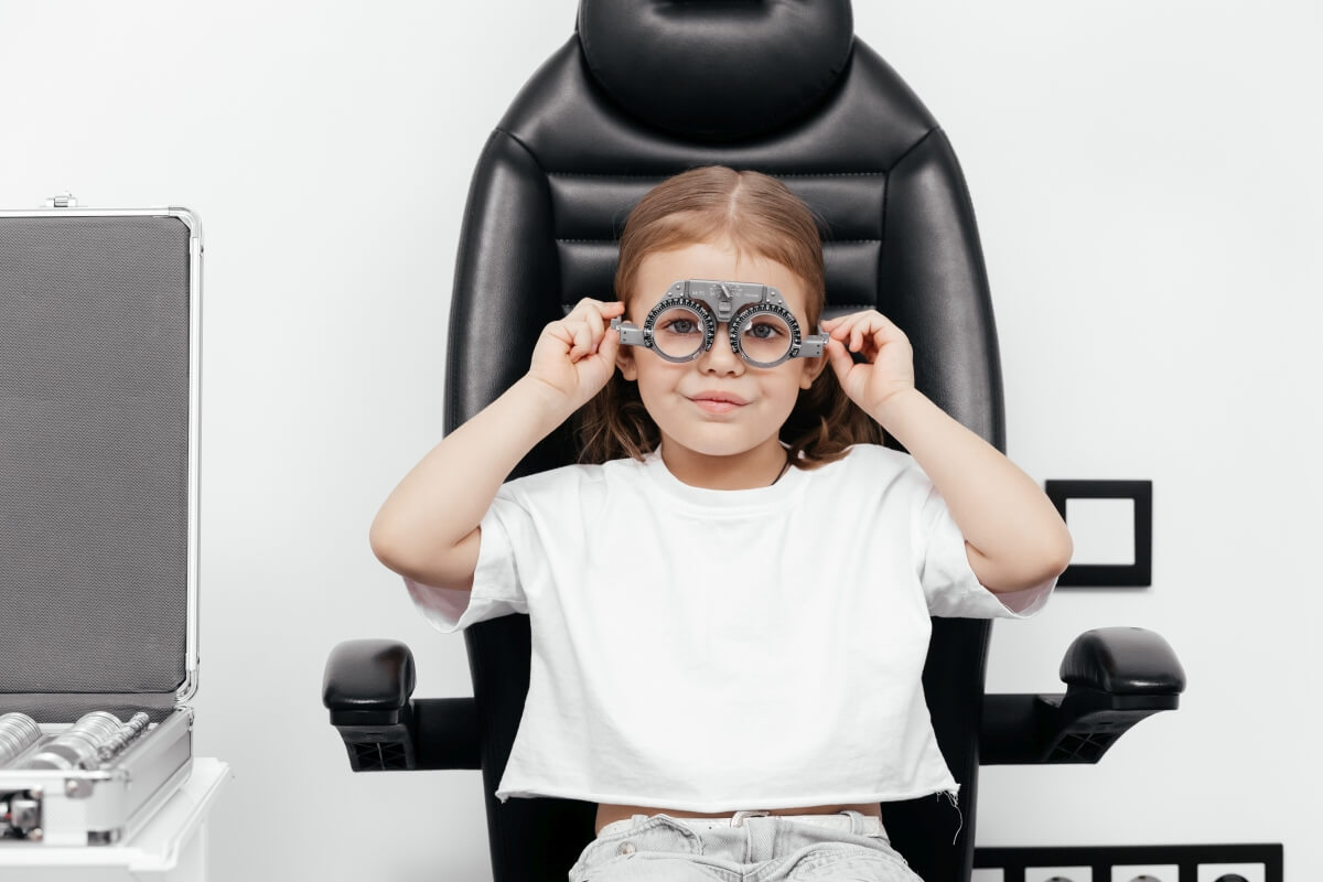 Dziecko na wizycie u okulisty dziecięcego, przymierzające okulary testowe.