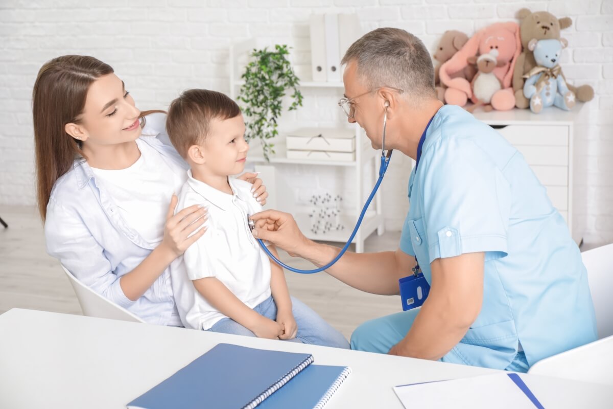 Kardiolog dziecięcy bada chłopca stetoskopem w obecności mamy.