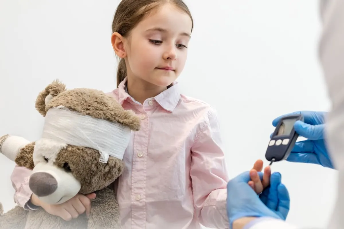 Dziewczynka trzyma pluszowego misia, a diabetolog dziecięcy mierzy jej poziom cukru.